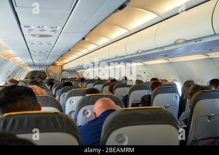 Passeggeri e equipaggio seduti sui sedili dell'aereo, vista dei passeggeri e degli assistenti all'interno della cabina Foto Stock