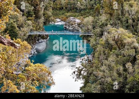 Gola di Hokitika, Nuova Zelanda - 14 luglio 2017: Una singola femmina si trova su un ponte sospeso sopra l'acqua blu e le rocce della gola di Hokitika Scen Foto Stock