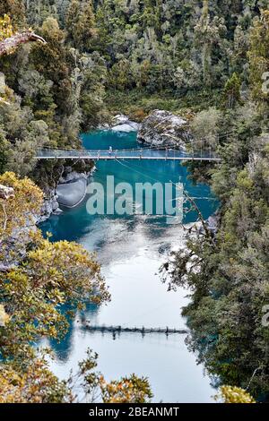 Gola di Hokitika, Nuova Zelanda - 14 luglio 2017: Una singola femmina si trova su un ponte sospeso sopra l'acqua blu e le rocce della gola di Hokitika Scen Foto Stock