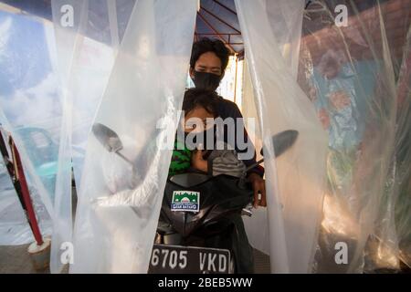 Giacarta, DKI Jakarta, IDN. 13 Aprile 2020. Persone che indossano maschere protettive che attraversano una motocicletta attraverso una camera di disinfezione presso un insediamento densamente popolato a nord di Giacarta, Indonesia. Alcuni residenti a Giacarta hanno iniziato a combattere seriamente il coronavirus (COVID-19) facendo un blocco e anche fornire vari modi, come la camera di disinfezione negli insediamenti stradali di accesso. Credit: Muhmmad Zaenuddin/ZUMA Wire/Alamy Live News Foto Stock