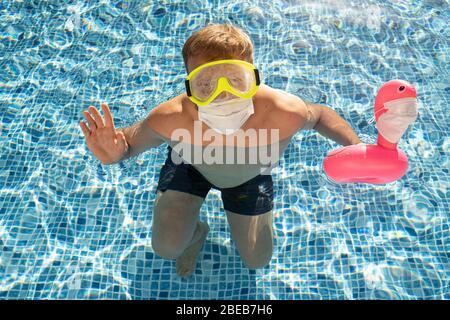 Maschio bianco caucasico in piscina con un giocattolo fenicottero in una maschera medica. Concetto di impatto dell'epidemia di Coronavirus su un'industria di viaggi per summ Foto Stock