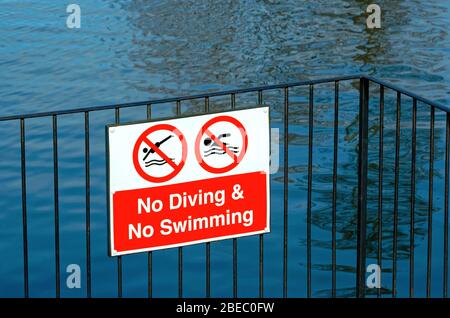 Un cartello appluso ad una recinzione che indica 'No Swimming' 'No Diving' da un lago Foto Stock