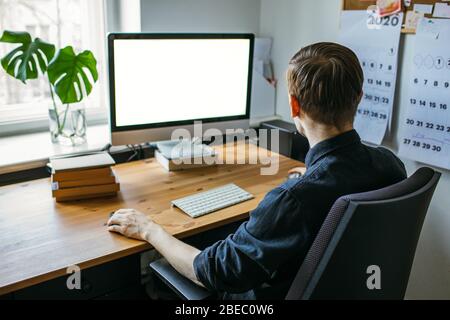 Uomo che lavora da casa. Computer con schermo vuoto per lo spazio di copia e le informazioni. Uomo d'affari da dietro la vista delle spalle. Un creativo Foto Stock