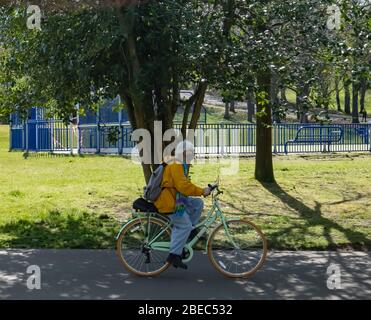 Glasgow, Scozia, Regno Unito. 13 aprile 2020. Il Lunedi di Pasqua durante il blocco pandemico coronavirus un ciclista indossando una maschera chirurgica facendo esercizio nel Queen's Park in un caldo pomeriggio di sole. Credit: Notizie dal vivo SKULLY/Alamy Foto Stock