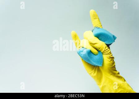 il guanto in gomma gialla tiene la spugna su sfondo bianco. il guanto in gomma gialla mostra il segno della roccia. Foto Stock