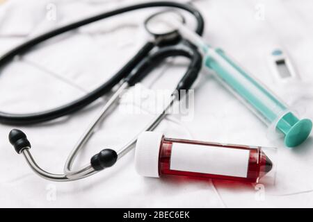 apparecchiatura medica e fiala per campioni di sangue con etichetta vuota con spazio per la copia di testo su un camoscione medico bianco, concetto di salute e medicina, foc selettivo Foto Stock