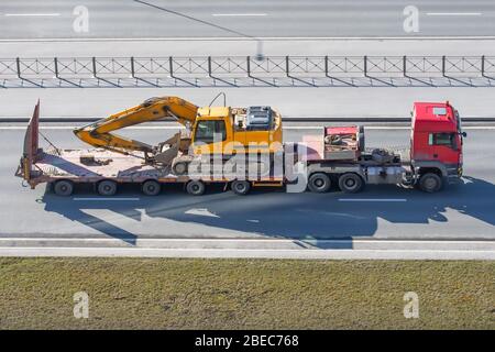 Escavatore su autocarro per trasporto con piattaforma lunga per rimorchio sull'autostrada in città Foto Stock