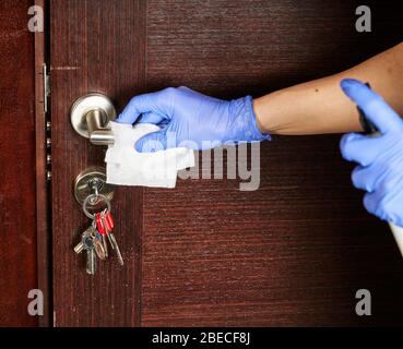 Disinfezione delle superfici da batteri o virus, pulizia manuale della maniglia della porta con disinfettante contro il coronavirus covid-19. Mano in blu con protezione Foto Stock