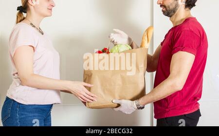 servizio di consegna smart food uomo in rosso uniforme consegna di cibo fresco al destinatario e giovane donna cliente che riceve l'ordine dal corriere a casa, espresso Foto Stock