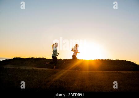 Due giovani donne che corrono insieme lungo le scogliere vicino all'oceano al tramonto Foto Stock