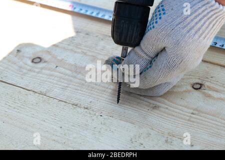 Avvitare la vite con un cacciavite elettrico in un pannello di legno, primo piano Foto Stock