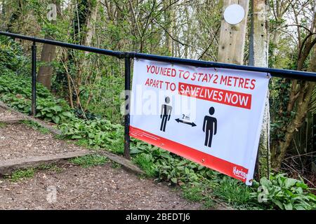 Scalini che portano al Parkland Walk, un sentiero naturalistico nel Nord di Londra, con un avviso di 'divaricamento sociale' sulle ringhiere, Regno Unito Foto Stock