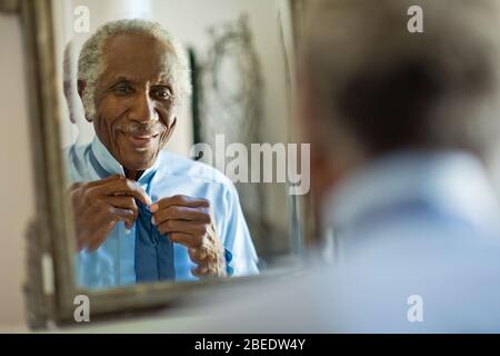 Felice uomo senior che legava la cravatta davanti a uno specchio Foto Stock
