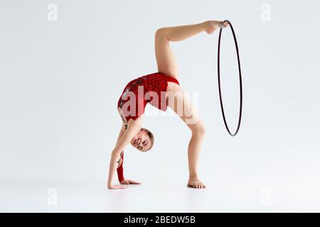 Giovane ginnastica flessibile che fa movimento complicato con cerchio, isolato su bianco Foto Stock