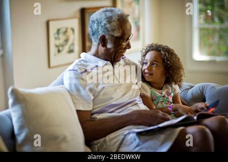 Buon uomo senior che legge un libro di storia con la sua giovane nipote Foto Stock
