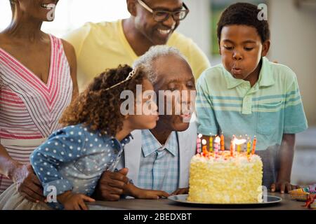 Uomo anziano che soffia fuori le sue candele di compleanno con la sua famiglia. Foto Stock