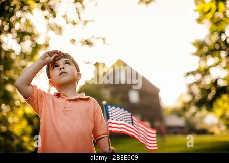 Giovane ragazzo saluta mentre tiene una bandiera americana Foto Stock