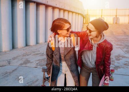 Due giovani donne felici a pelo corto che si rotolano insieme, tenendo i loro skateboard Foto Stock