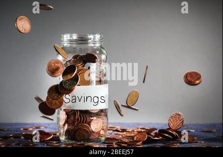 Monete che cadono su un vaso di risparmio pieno di sterline britanniche Foto Stock