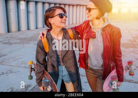 Due giovani donne felici a pelo corto che si rotolano insieme, tenendo i loro skateboard Foto Stock