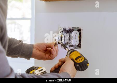 Il lavoro di installare prese elettriche con fili elettrici e connettore installato nel muro a secco di pannelli in gesso cartonato Foto Stock