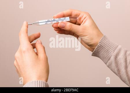 closeup donna mani tenendo un termometro di vetro con temperatura elevata al di sopra di trentotto. sintomi coronavirus, infezione Foto Stock