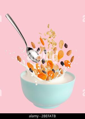 Muesli ingredienti volare sopra la ciotola con il latte spruzzato. Isolato su sfondo rosa. Foto Stock