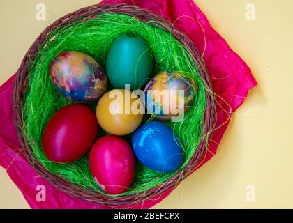Nido d'erba verde in un cesto con uova di Pasqua colorate, uova dipinte multicolore, tradizione pasquale, concetto di celebrazione Foto Stock
