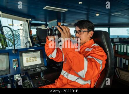 Ufficiale di ponte filippino sul ponte di nave o di nave che guarda attraverso binocoli Foto Stock