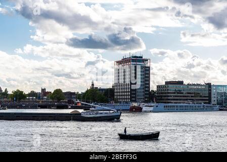 Amsterdam, Paesi Bassi - 7 settembre 2018: Grande nave da carico e un uomo solo in una barca che naviga sul fiume ad Amsterdam, Paesi Bassi Foto Stock