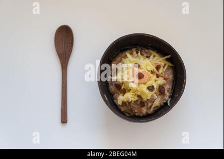 Vista superiore della deliziosa e nutriente colazione vegana farinata d'avena porridge con mela grattugiata e burro di arachidi, servita in ciotola di cocco. Foto Stock