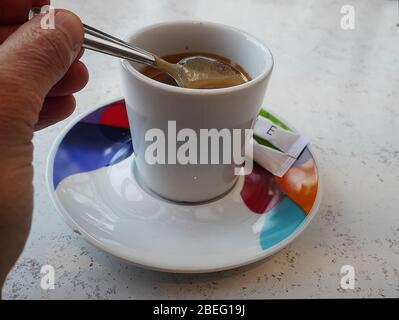 Bere un espresso servito su un piattino colorato in un bar. Cucchiaio e zucchero Foto Stock