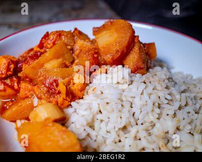 Primo piano di curry vegetale piccante e sano riso integrale marrone in una ciotola rossa Foto Stock