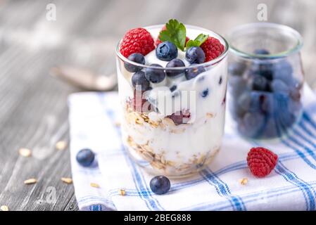 Yogurt bianco in vaso di vetro con lamponi e mirtilli su tovkin. Foto Stock