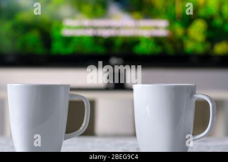 Tazze da caffè con un televisore con un documentario e sottotitoli sulla natura in background Foto Stock