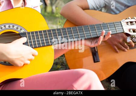 Bambina e donna adulta suonano insieme la chitarra in campagna. Primo piano delle mani. Foto Stock