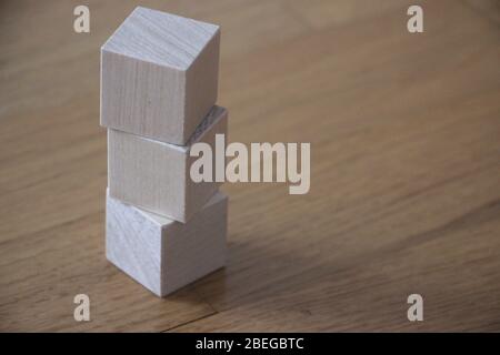 Tre cubetti di legno si sono fatti vertire verticalmente sullo sfondo del tavolo Foto Stock