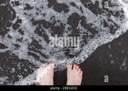 I piedi di una donna sulla spiaggia di sabbia nera di Hana, Maui, Hawaii Foto Stock