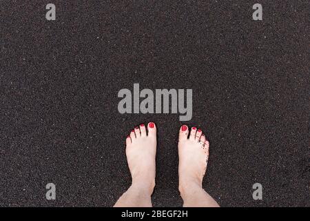 I piedi di una donna sulla spiaggia di sabbia nera di Hana, Maui, Hawaii Foto Stock