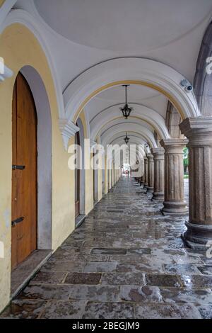 Passerella in pietra coperta con archi e colonne di un edificio coloniale adiacente al parco centrale di Antigua, Guatemala Foto Stock