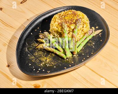 Risotto vegano con Asparagi e Curry (senza burro), su un piatto scuro su un tavolo di legno. Foto Stock