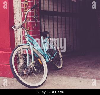 Bicicletta blu turchese appoggiata contro una parete rossa brillante vicino ad un vicolo. Foto Stock