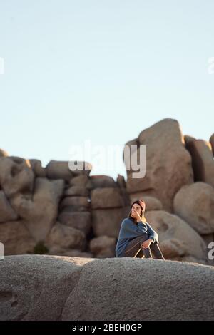 Giovane donna seduta su rocce contemplando Foto Stock