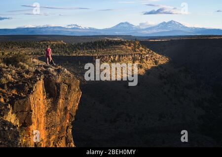 Donna in piedi sul bordo della scogliera che domina il canyon e le montagne Foto Stock