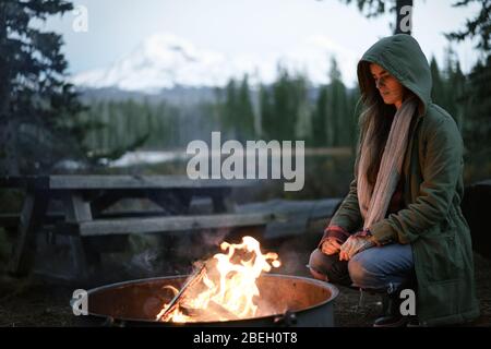 Donna accoccolata dal fuoco con cappuccio in su Foto Stock