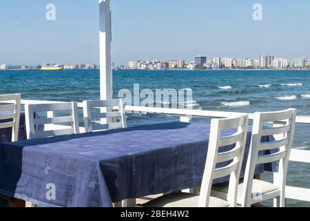 Ristorante sul molo di Vlore, Albania sul Mar Ionio in una giornata estiva soleggiata, tavoli coperti di tovaglie blu, sedie bianche. Linea costiera di Vlora Foto Stock