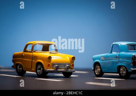 Due giocattoli cas uno blu e uno giallo colorato su fondo blu e asfalto strada. Foto Stock