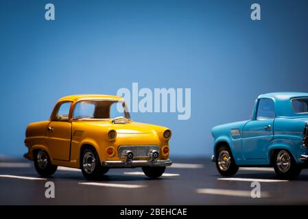 Due giocattoli cas uno blu e uno giallo colorato su fondo blu e asfalto strada. Foto Stock