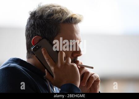 Ritratto di uomo che fuma sigaretta mentre sul suo telefono. Foto Stock