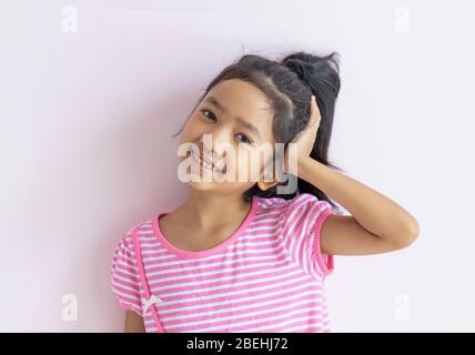 Ritratto di una bambina asiatica che indossa un abito a righe rosa e bianco. Il bambino ha usato una mano sinistra per prendere la testa e sorridere con felicità. Foto Stock
